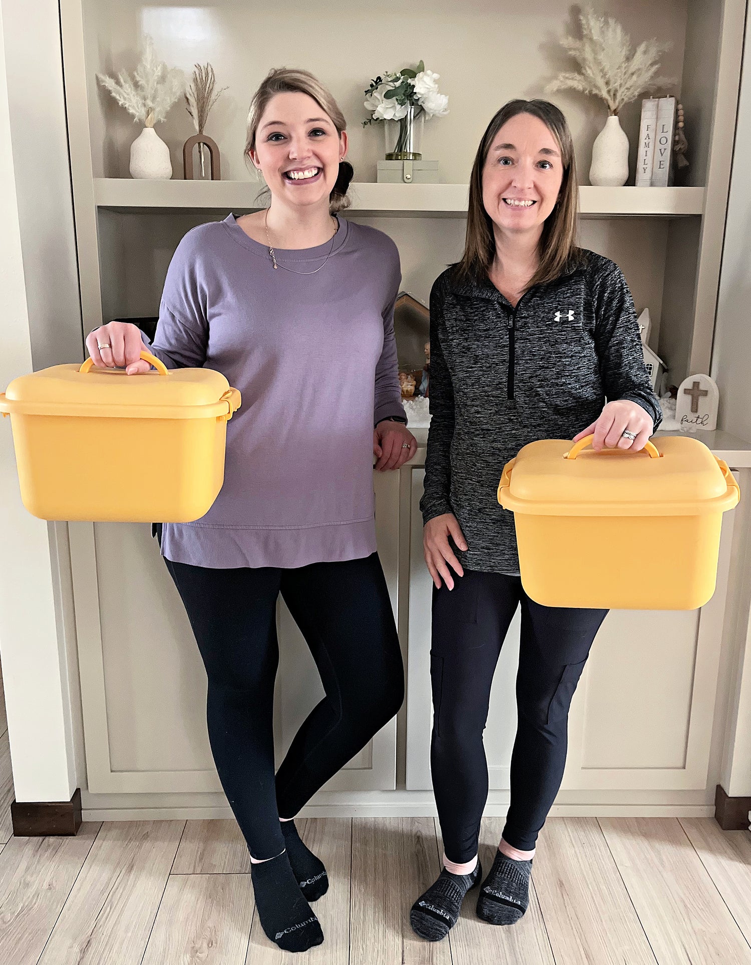 Two ladies standing next to each other holding yellow bins by the handle.