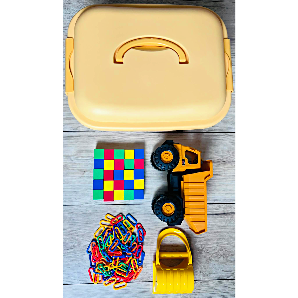 A yellow bin, a dump truck, colorful foam blocks, plastic rainbow links, and a yellow hand shovel.