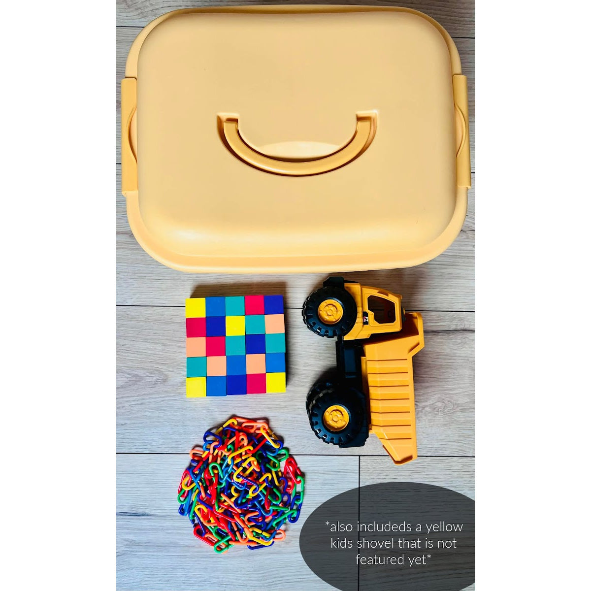 Yellow toy toolbox with colorful blocks, toy truck, and rubber band toy on a wooden surface.