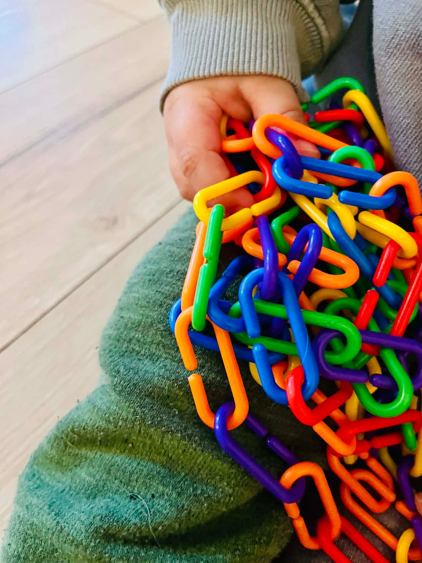 Colorful plastic links held by a child on a wooden floor.