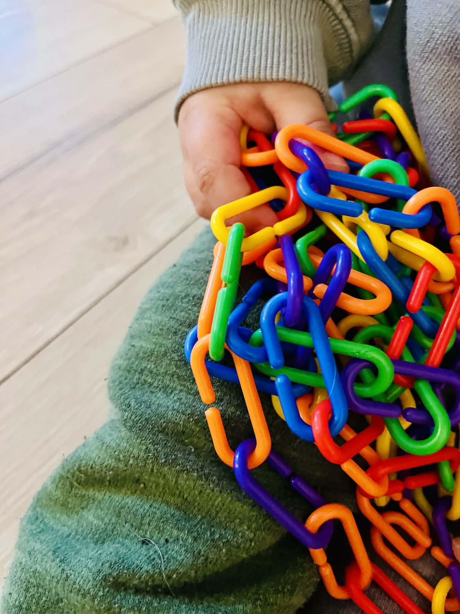 Colorful plastic links held by a child on a wooden floor.