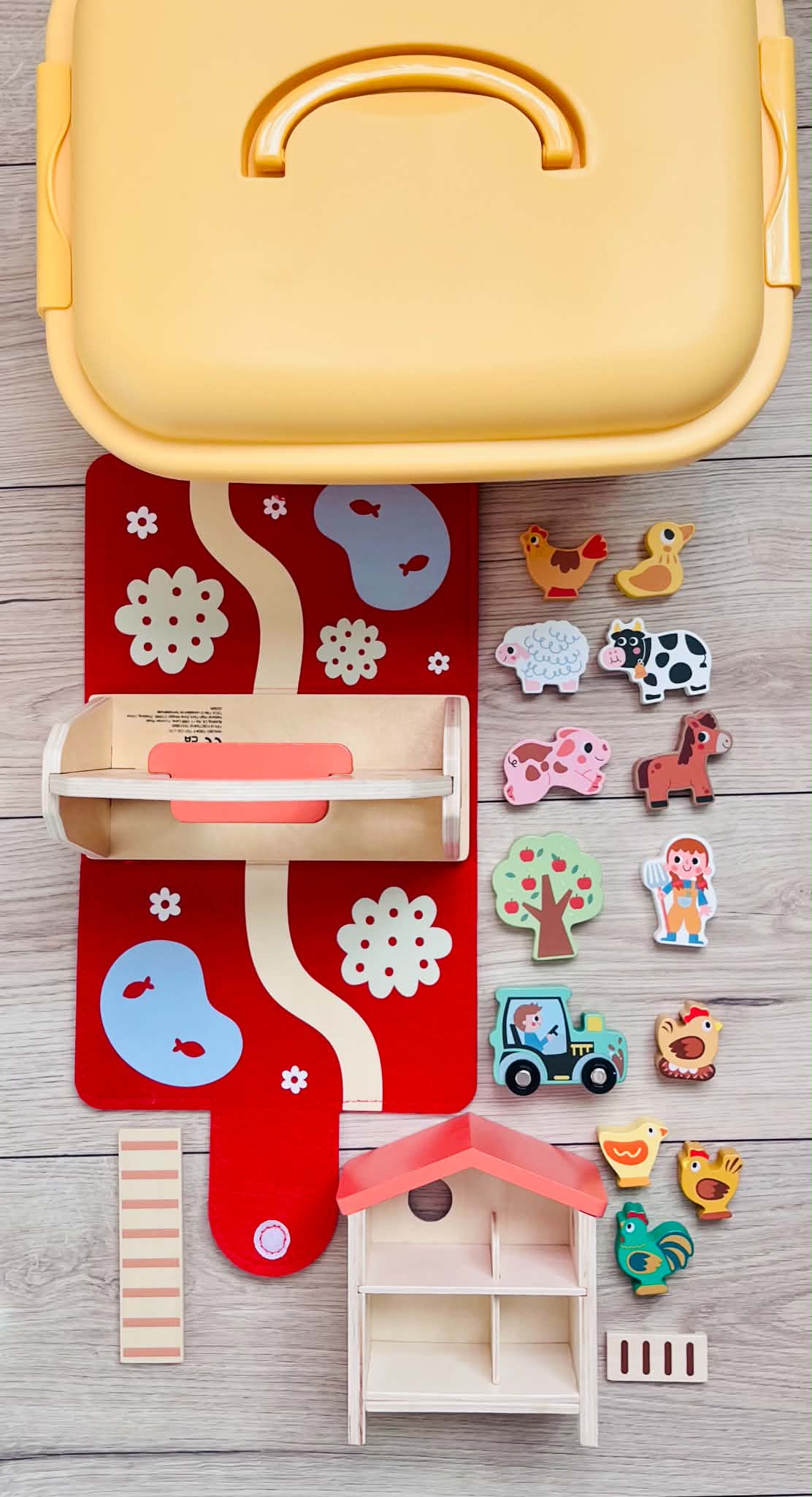 A yellow bin with wooden farm animals, a barn, a green tractor, and a chicken coop.