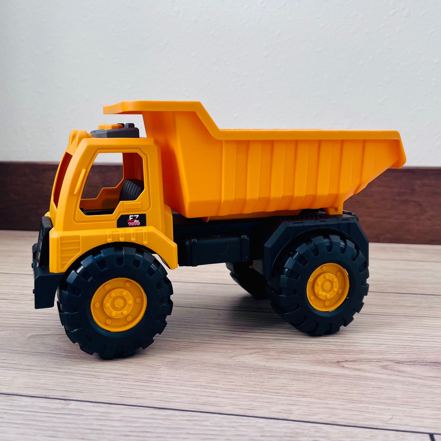 Yellow toy dump truck on a wooden surface with a neutral background